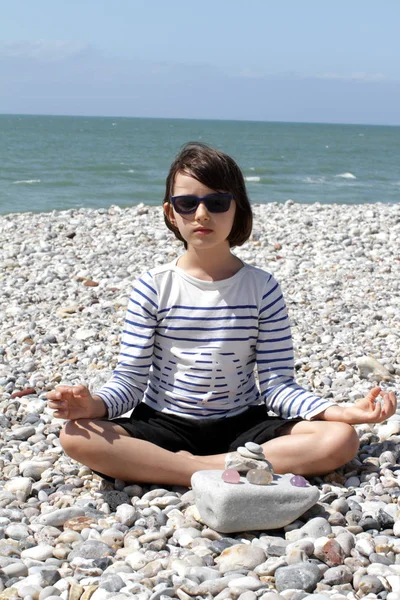 Bambino con occhiali da sole yoga che prega con cristalli di quarzo sulla spiaggia — Foto Stock