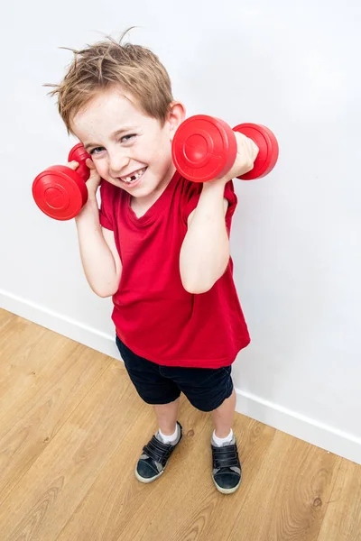 Sorrindo menino expressando orgulho divertido, levantando halteres para crescer — Fotografia de Stock