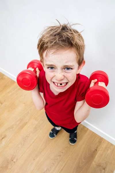 Божевільний хлопчик з вільними зубами, що піднімає гантелі з зусиллями — стокове фото
