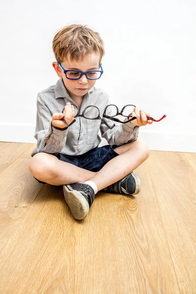 多くの眼鏡や木製の床を選ぶことに疑問を持つ幸せな少年は — ストック写真