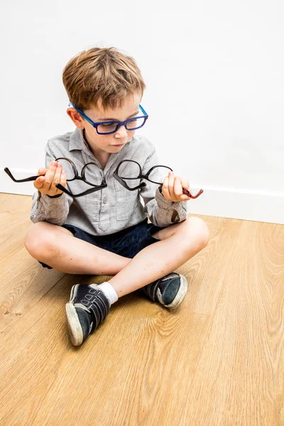 Niño feliz con varias gafas en las manos vacilantes, piernas cruzadas —  Fotos de Stock