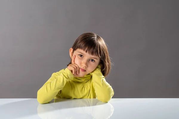 Aburrida niña sosteniendo su cabeza sobre sus manos, luciendo seria — Foto de Stock