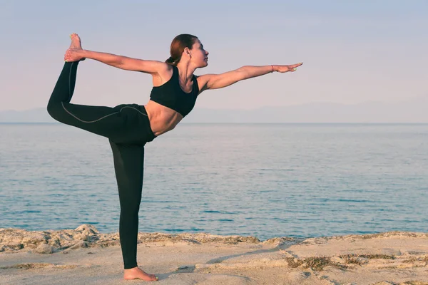 European woman practicing fitness yoga workout on the coast at sunset. Training on sea and mountains background. Concept of a healthy lifestyle and individual outdoor sports while social distancing.