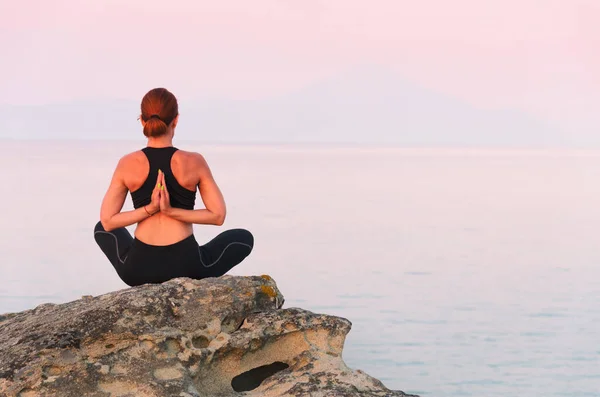European woman practicing fitness yoga workout on the coast at sunset. Training on sea and mountains background. Concept of a healthy lifestyle and individual outdoor sports while social distancing.