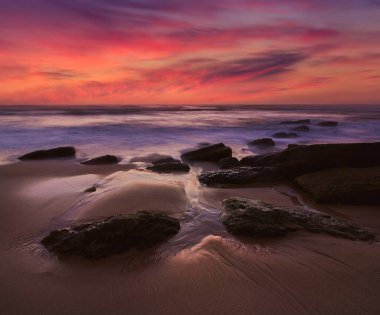Atlantik Okyanusu 'nda gün batımının inanılmaz manzarası. Dramatik gökyüzü, deniz manzarası, kumlu sahil ve taş. Uzun pozlama görüntüsü. Portekiz. Doğa arkaplanı kavramı.