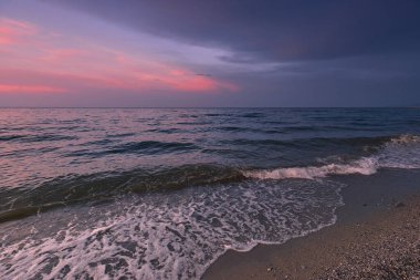 Gün batımında kıyıda. Sörf dalgası bir deniz kumsalını kaplıyor. Yunanistan. Akdeniz 'de. Doğa arkaplanı kavramı.