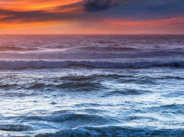 Gün batımında okyanus kıyısının inanılmaz romantik deniz manzarası. Renkli bulutlu gökyüzü ve köpüklü dalgaların manzarası. Vahşi yaşamla uyum kavramı. Portekiz.