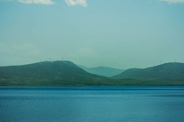 Arkasında dağlar olan güzel mavi bir okyanus. Dağlar yeşil ağaçlarla kaplı ve su sakin.