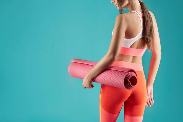 Esmer kızın elinde yoga minderi var.