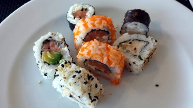 Beyaz bir plaka üzerinde taze, renkli suşi yedi parçalar.