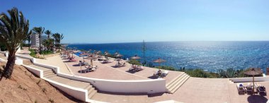 Mayorka, İspanya - 18 Haziran 2018: İspanya 'nın Mayorka kıyısındaki bir tatil köyünde dinlenin. İnsanlar deniz kıyısındaki palmiye ağaçlarının altında güneşleniyorlar..