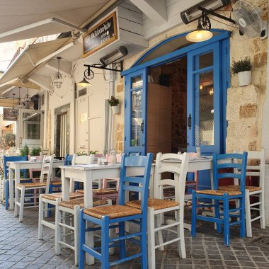 Chania, Girit - 22 Haziran 2019: İnsansız Yunan restoranı. Mavi beyaz sandalyeler ve masalar dışarıda..