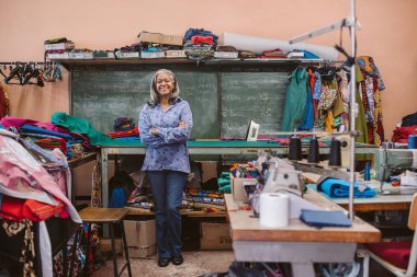 Portre renkli malzeme ve dikiş ekipman çevrili bir tablo tarafından geçti kollarını ile onun atölyesinde ayakta gülümseyen bir olgun terzi