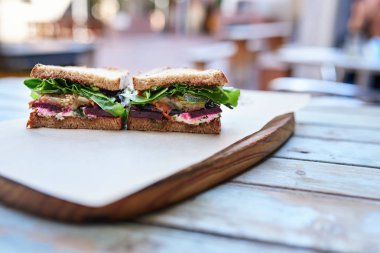 Yarısını kesip bir kaldırım kafe, ahşap bir masa üzerinde dinlenme çeşitli organik sebze ile zanaat sandviç