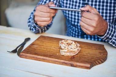 Onun lezzetli fıstık ezmesi ve banana açık resmi karşı karşıya sandviç almak onun smartphone kullanarak bir bistro masada oturan genç adam