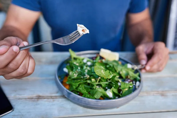 Young man sitting alone at a bistro table eating a delicious plate of mixed salad with a knife and fork