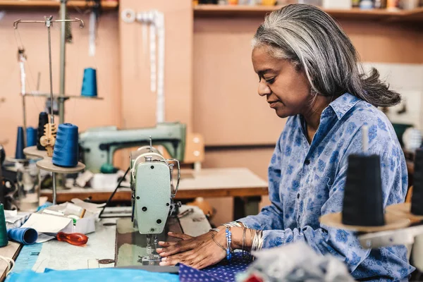 彼女の店で働きながらカラフルな生地の部分をステッチ ミシンで座っている成熟した女性の裁縫師 — ストック写真