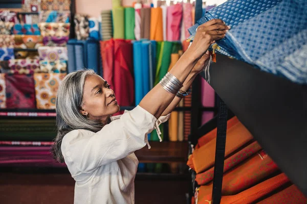 Smiling Mature Woman Looking Rolls Colorful Textiles Shelf While Shopping — Stock Photo, Image