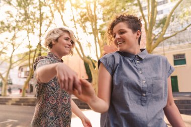 Gülüyor ve el ele birlikte dışında şehrin bir sokakta güneşli bir günde dans genç lezbiyen çift gülümseyen