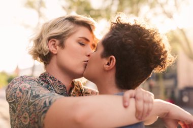 Sarılma ve romantik bir paylaşım genç lezbiyen çift birlikte güneşli bir gün dışarı zevk bir şehir cadde üzerinde dururken öp. 