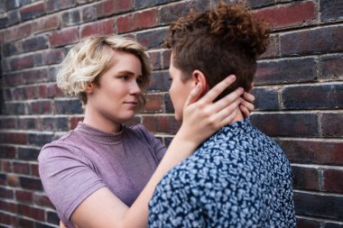 Sevgi genç lezbiyen çift birlikte bir tuğla duvarın dışında önünde ayakta iken birbirlerinin gözlerine bakıyor