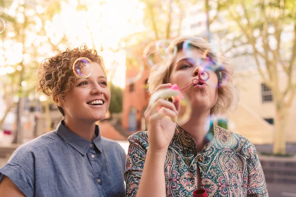 微笑的年轻最好的朋友吹气泡与泡沫魔杖 而享受一个有趣的一天一起在城市 — 图库照片