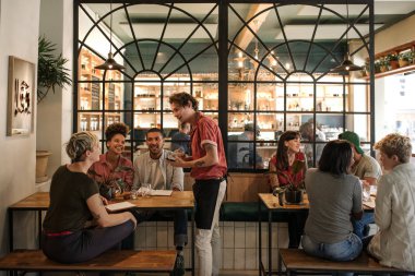 Genç garson emir birlikte bir restoran masada oturan müşteriler farklı bir grup gülümseyen