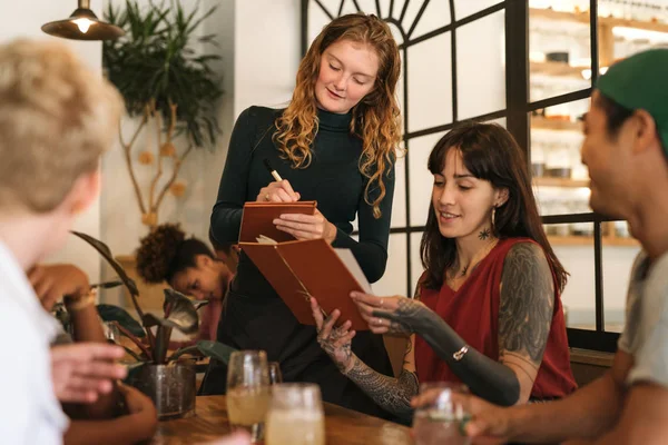 Onun menü düzeni gülümseyen bir garson kıza vererek sipariş bir bistro masa arkadaşlarınızla oturup dövmeli genç kadın