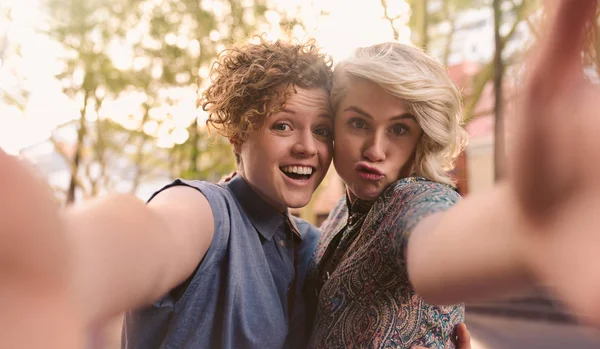 微笑的年轻女同性恋夫妇站在一起在城市的街道上做鬼脸 并采取自拍 而享受一天出来 — 图库照片
