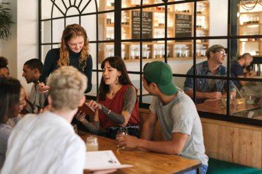 Trendy bir bistro menüler okuma ve garsonluk sipariş bir masada oturan farklı genç arkadaş grubu