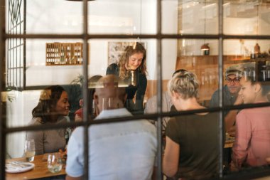 Garson garson gülümseyerek lezzetli taze gıda birlikte modaya uygun bir bistro içinde bir masada oturan bir müşteri grubu için yapılmış