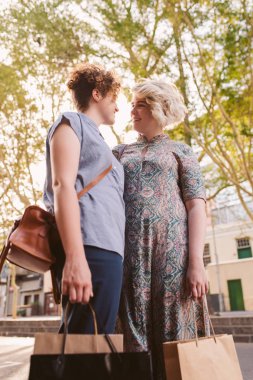 Genç lezbiyen çift ayakta birlikte bir gün dışarı tadını çıkarırken alışveriş çantaları taşırken kentin bir sokakta gülümseyen