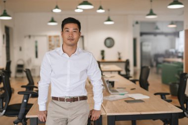 Kendine güvenen Genç Asyalı işadamı tek başına büyük bir modern ofiste çalışırken bir tablo karşı yaslanmış