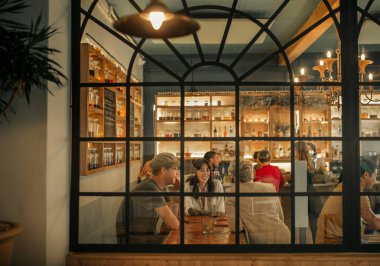 Grup gülümseyen arkadaşıyla konuşuyor ve birlikte bir trendy bar içinde windows tarafından bir masada otururken gülüyor 