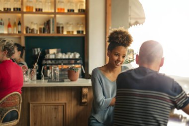 Gülümseyen genç Afrikalı-Amerikalı kadın bir erkek arkadaşı ile konuşurken trendy bir barda bir pencerenin yanında oturan