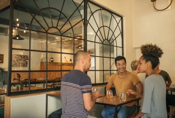 不同的一群微笑的年轻朋友坐在一起 在一个时髦的酒吧的桌子上喝酒 一起聊天 — 图库照片
