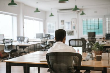 Bir dizüstü bilgisayarda çalışma ve rahat bir ofiste onun masasında otururken evrak işleriyle bir anonim iş kişinin arka görünümü 