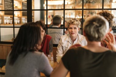 Genç kadın arkadaşlar trendy bar içecekler ve birlikte konuşurken bir masada oturan farklı grup