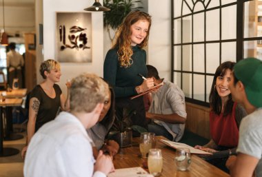 Genç garson emir bir Bistro bir masada oturan müşteriler farklı bir grup gülümseyen