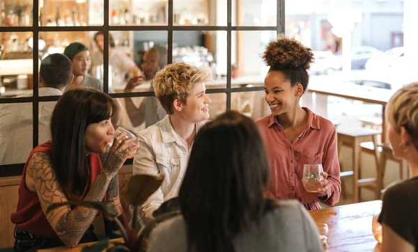 不同的一群年轻的女性朋友一起欢笑和交谈 而坐在一张桌子上的时髦酒吧喝 — 图库照片