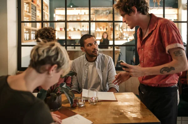 Grup çeşitli genç arkadaşıyla birlikte şık bir restoranda bir masada otururken bir garson yemek siparişi 