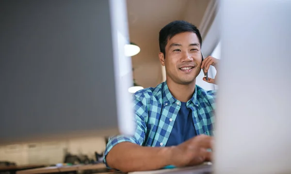 年轻的亚洲设计师微笑着在一个现代化的办公室坐在办公桌前 用手机和电脑工作 — 图库照片