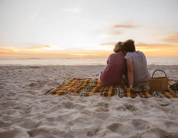 ビーチで一緒に毛布に坐っている間ロマンチックな夕日を見て コンテンツ若いレズビアンのカップルのバックミラー — ストック写真