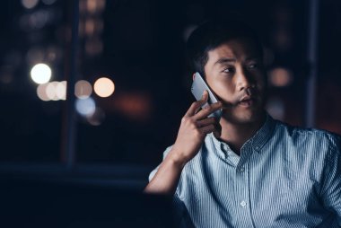 Genç Asyalı işadamı arka planda parlayan şehir ışıkları ile gece geç saatte ofisinde çalışırken bir cep telefonunuzun konuşma