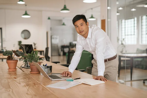 ノート パソコンでオンラインで作業して 書類上の近代的なオフィスに彼の机に寄りかかって集中若いアジア系のビジネスマンの肖像画 — ストック写真