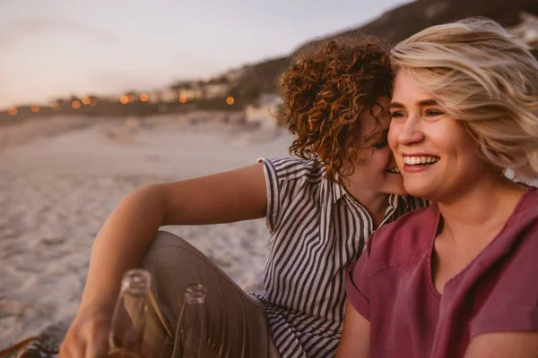 笑って話して 一緒にロマンチックな夕日を見て砂浜に座って飲み物を持つ若いレズビアンのカップル — ストック写真