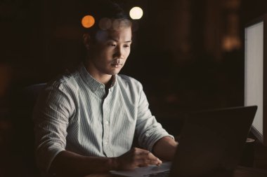 Genç Asyalı işadamı online geç saatte bir ofiste onun masasında akşam arka planda parlayan şehir ışıkları ile çalışma