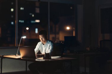 Karanlık bir ofiste onun masasında gece şehir ışıkları içinde belgili tanımlık geçmiş ile otururken bir dizüstü bilgisayarda çalışan genç Asya iş adamı