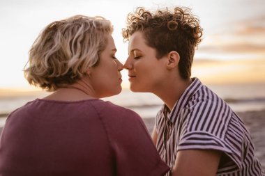 Sevgi genç lezbiyen çift birlikte gün batımını izlemek kumlu bir plaj üzerinde otururken romantik bir an zevk
