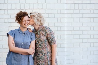 Gülümseyen kız arkadaşı birlikte bir tuğla duvarın dışında önünde ayakta iken yanağından öpmek sevgi genç kadın